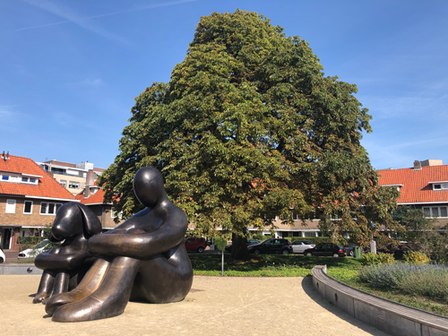 Groot brons beeld van zittend persoon en hond voor een grote boom