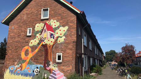 Beschilderde zijkant van een woning met daarop boomhut in een boom en spelende dieren