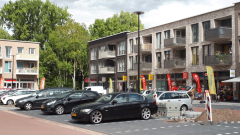 Parkeerterrein met geparkeerde auto's en daarachter winkels met appartementen
